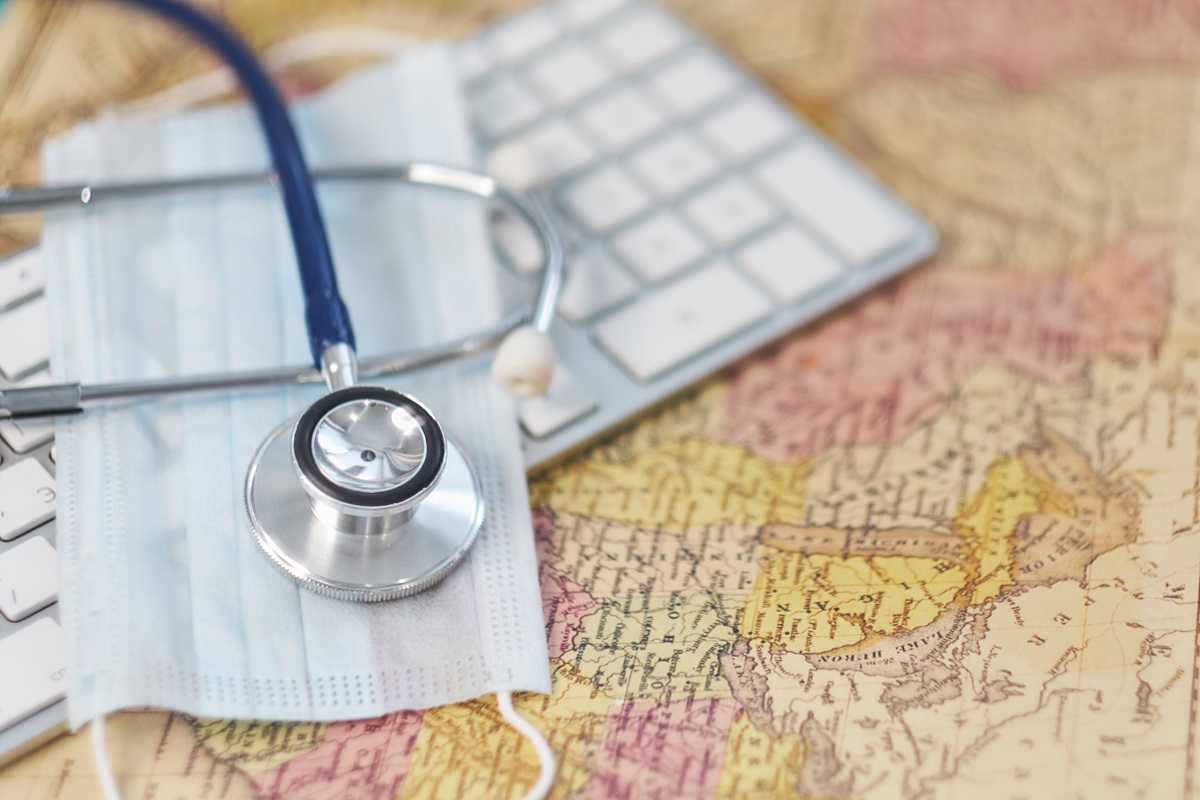 Keyboard, medical stethoscope and a protective mask on a geographical map.